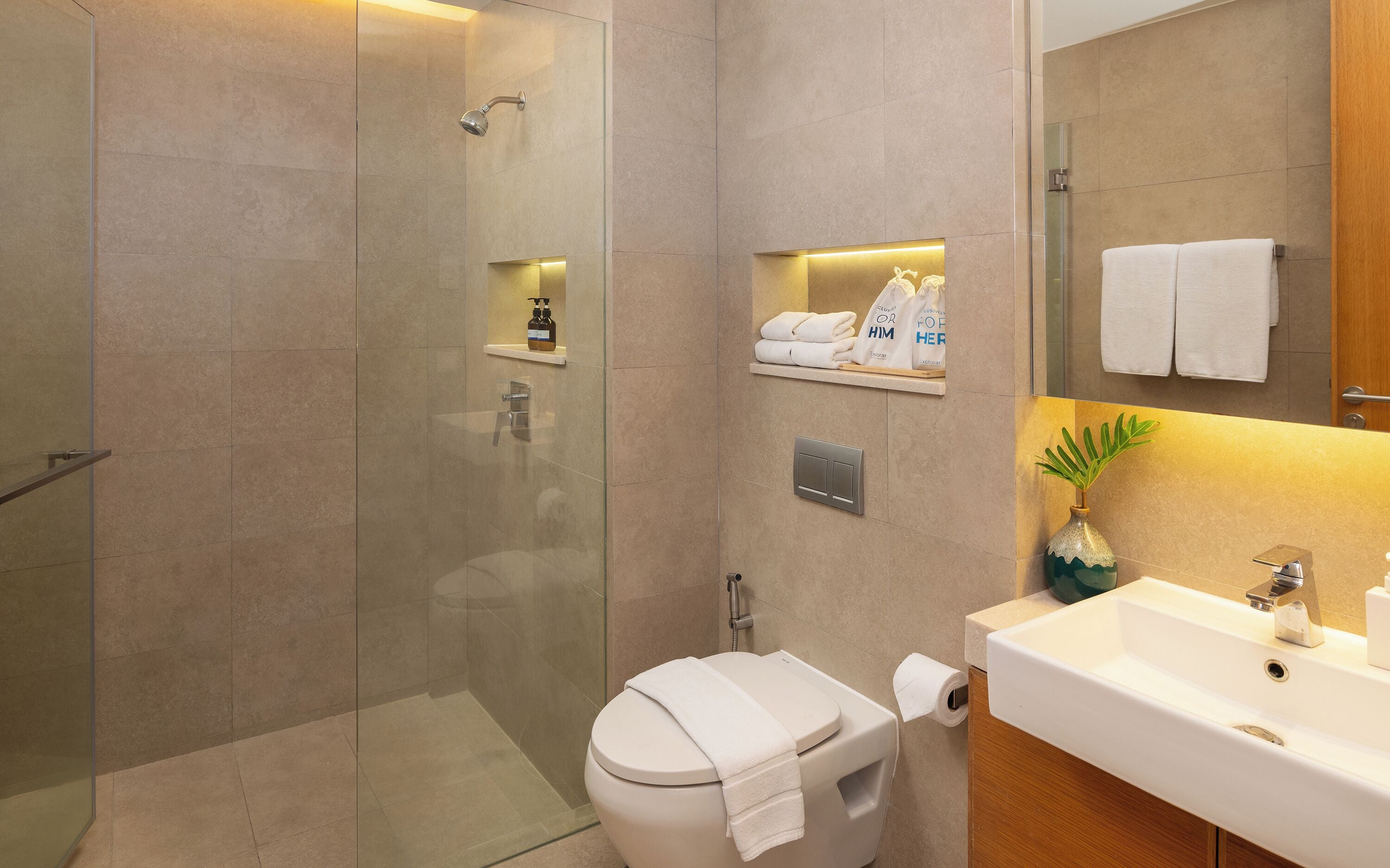 Une salle de bain moderne avec une douche à parois de verre, des toilettes avec une serviette posée sur le siège, un lavabo avec un miroir et une étagère contenant des articles de toilette.