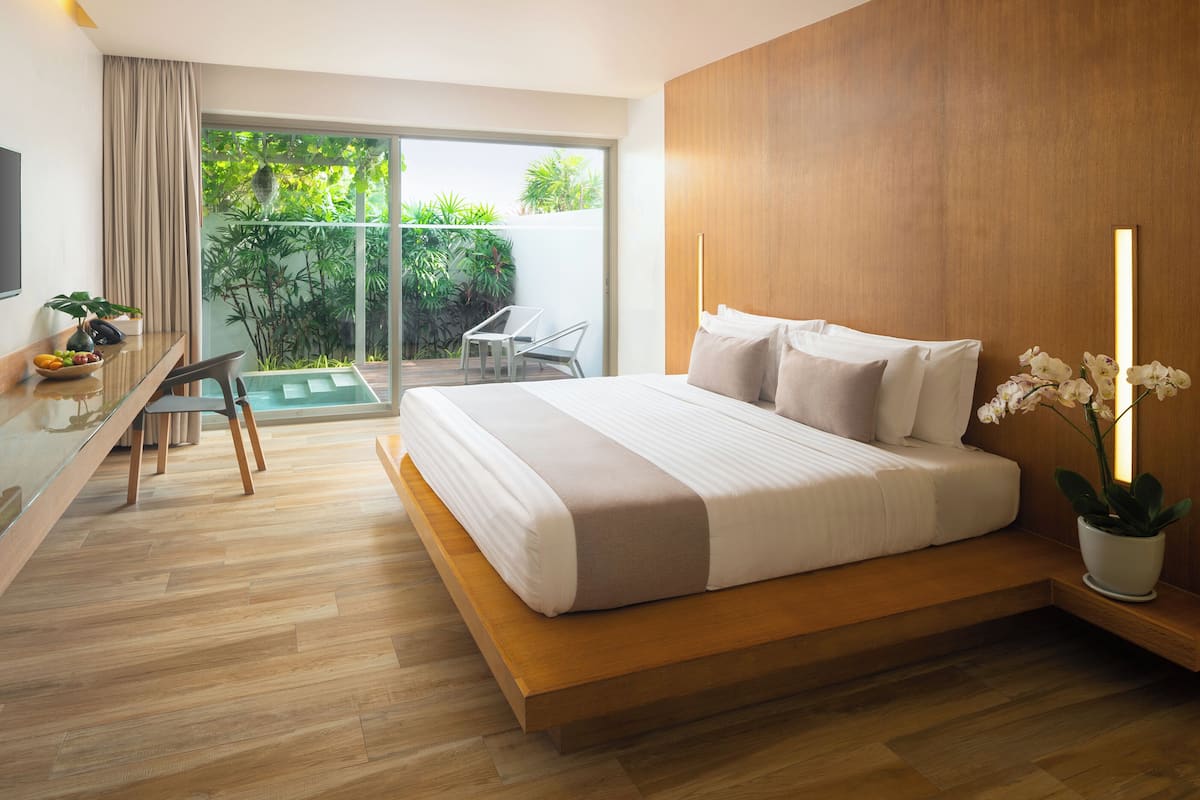 Una habitación de hotel moderna con una cama grande, un escritorio con computadora, un televisor y un balcón con plantas.