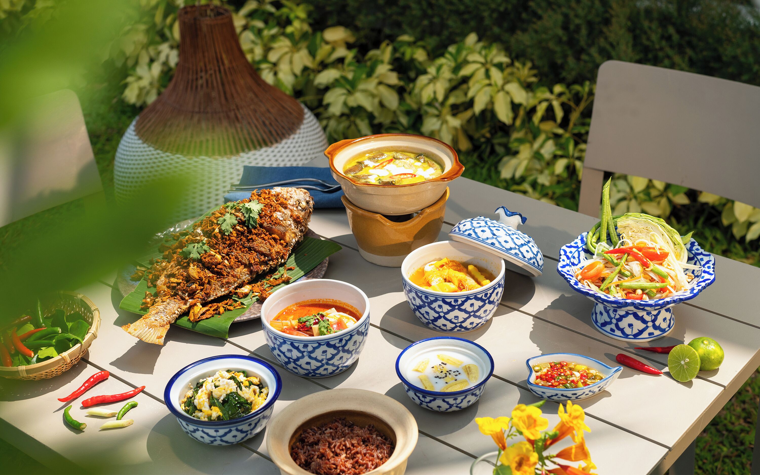 A table with various dishes, including a whole fish, bowls of soup, and a salad.
