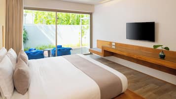Een moderne hotelkamer met een groot bed, een aan de muur bevestigde televisie, een klein zitgedeelte met een tafeltje en uitzicht op groen.