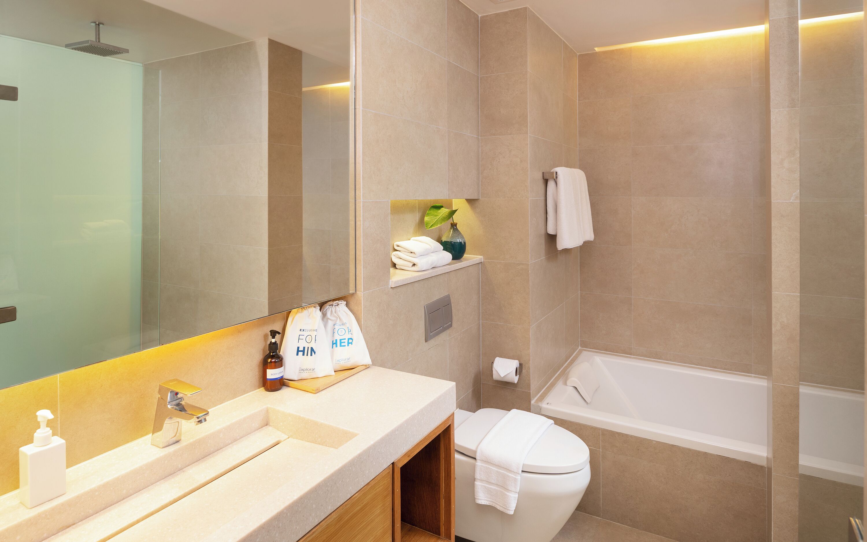 A bathroom with a sink, mirror, toilet, and bathtub. There are towels and toiletries on the counter.