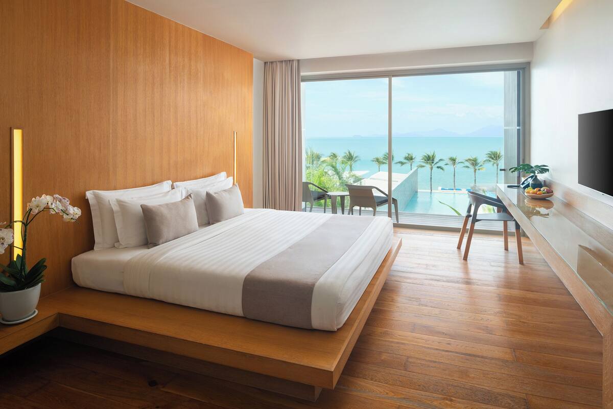Habitación de hotel moderna con una cama grande, un escritorio y vistas al océano.