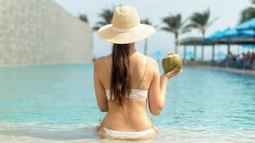 Une personne dans une piscine, portant un chapeau de paille et un bikini, et tenant une noix de coco.