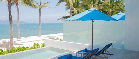 Zona junto a la piscina con sillones de descanso y sombrillas, con vistas al mar.