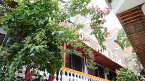 Un edificio con fachada de blanco y negro, un balcón con barandilla blanca y plantas florecientes de color rosa.