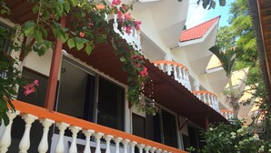 Un edificio con fachada blanca, un balcón con balaustradas blancas y un techo rojo.
