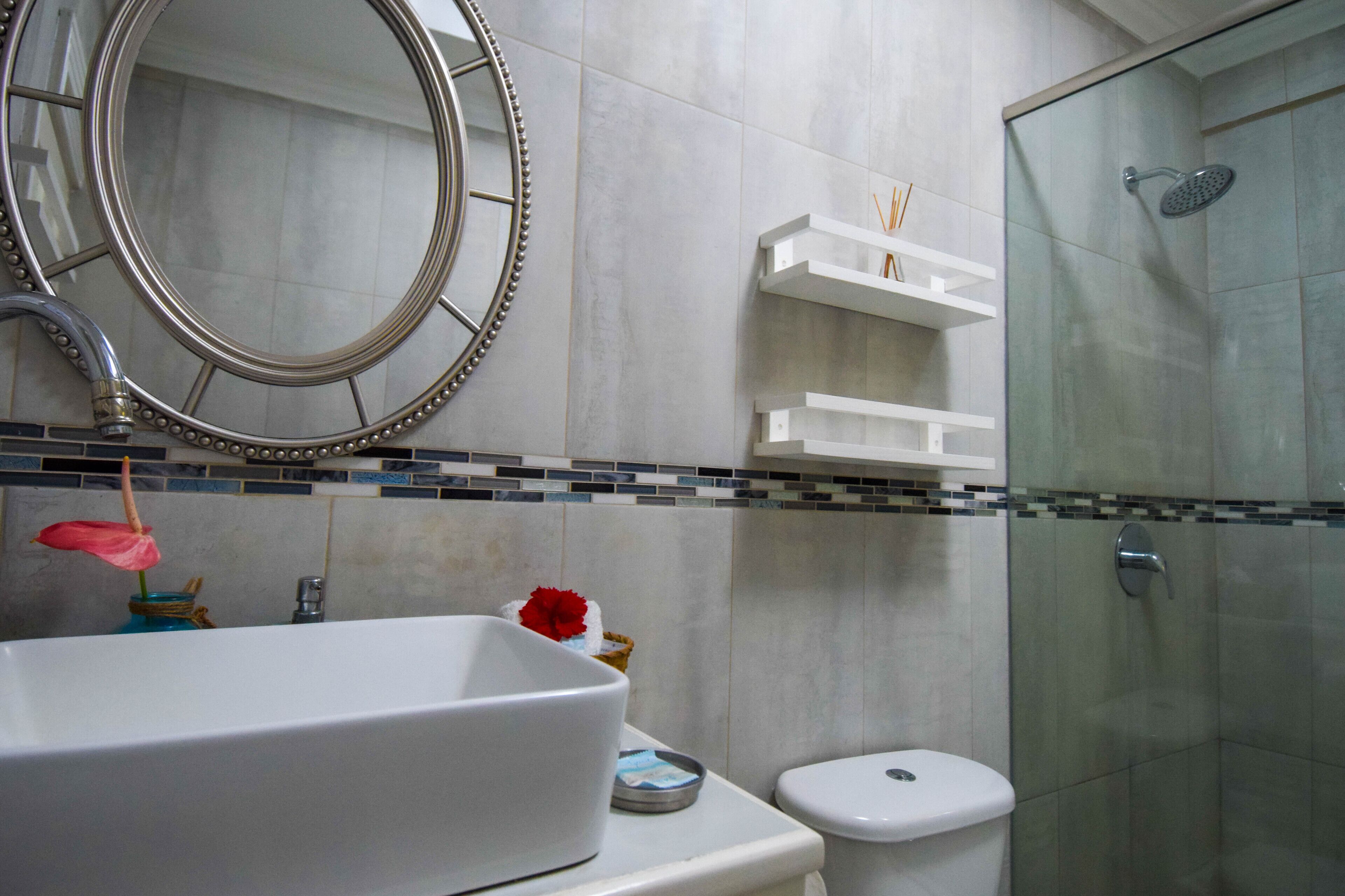 Un baño con un espejo grande, un lavamanos blanco, un inodoro y una ducha con mampara de vidrio.