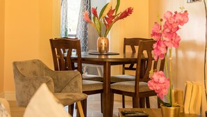 A dining area with a wooden table, chairs, and a vase of flowers. - Sea Piton View Apartment (Soufrière)