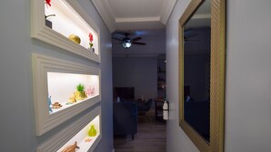 A hallway with shelves displaying various decorative items, a ceiling fan, and a mirror on the right. - Sea Piton View Apartment (Soufrière)