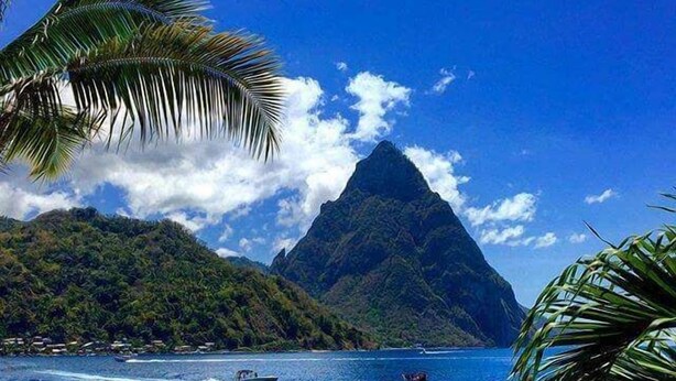 A beach with clear blue water, a boat, and a mountain in the background. - Sea Piton View Apartment (Soufrière)