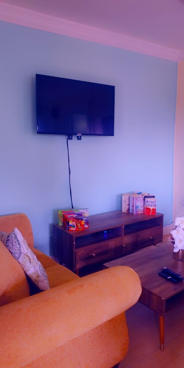 Una sala de estar con un televisor de pantalla plana montado en la pared, una mesa de centro de madera y un sofá naranja.