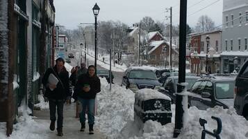 Uma rua coberta de neve com edifícios de ambos os lados, uma bicicleta encostada a um poste e carros estacionados.