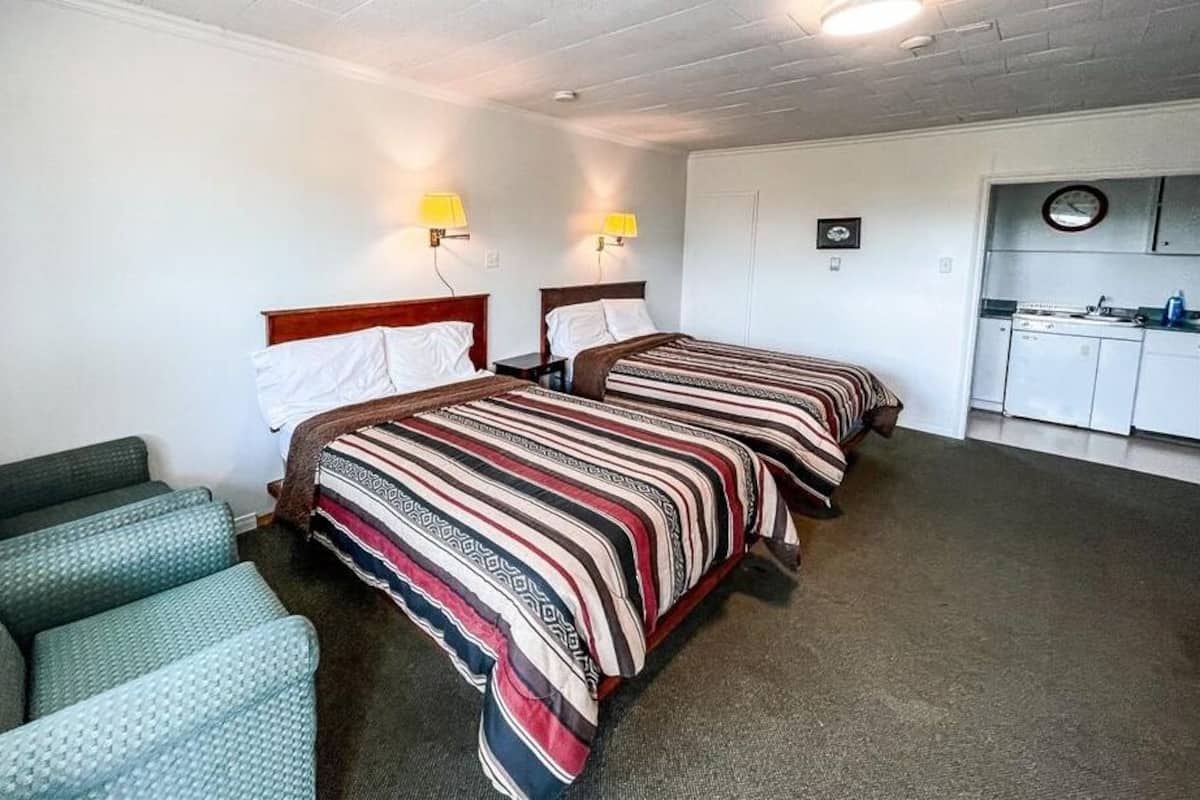 A hotel room with two beds, a kitchenette, and a seating area.
