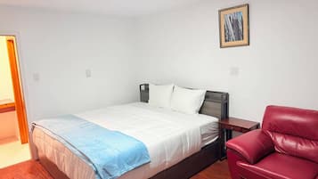 A bedroom with a bed, a red chair, a wooden floor, and a painting on the wall.
