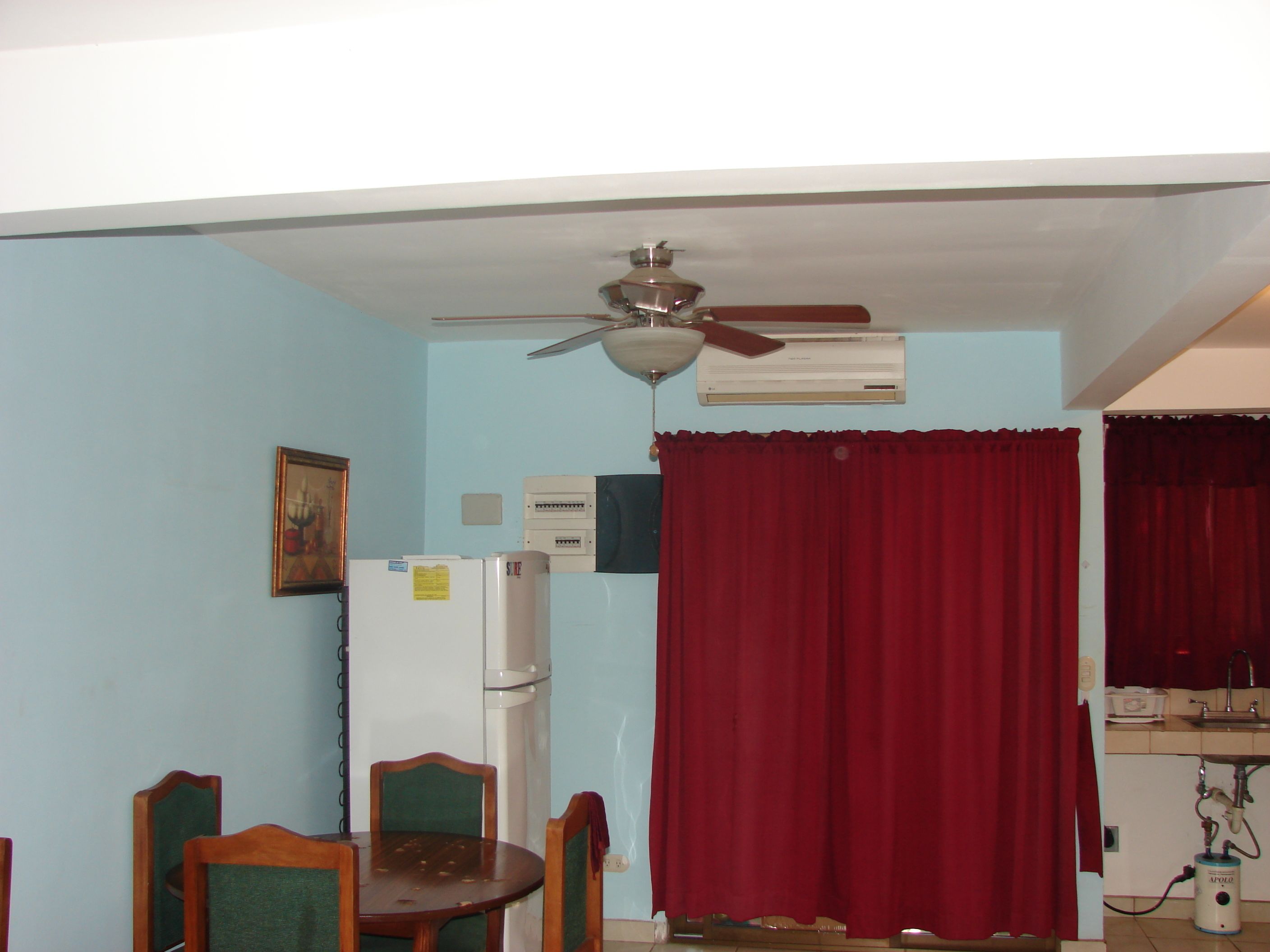 A dining area with a table and chairs, a ceiling fan, an air conditioning unit, and a red curtain.