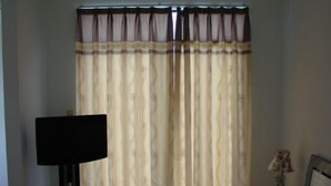 Un dormitorio con cama, televisión y cortinas.