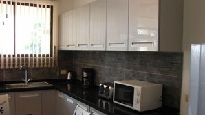 Una cocina con armarios blancos, encimera negra, microondas, cafetera y lavaplatos.