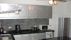 Una cocina moderna con gabinetes grises, encimera negra, refrigerador de acero inoxidable, microondas y cafetera.