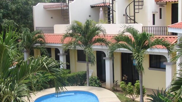 Un edificio con varios balcones, piscina y abundante vegetación.