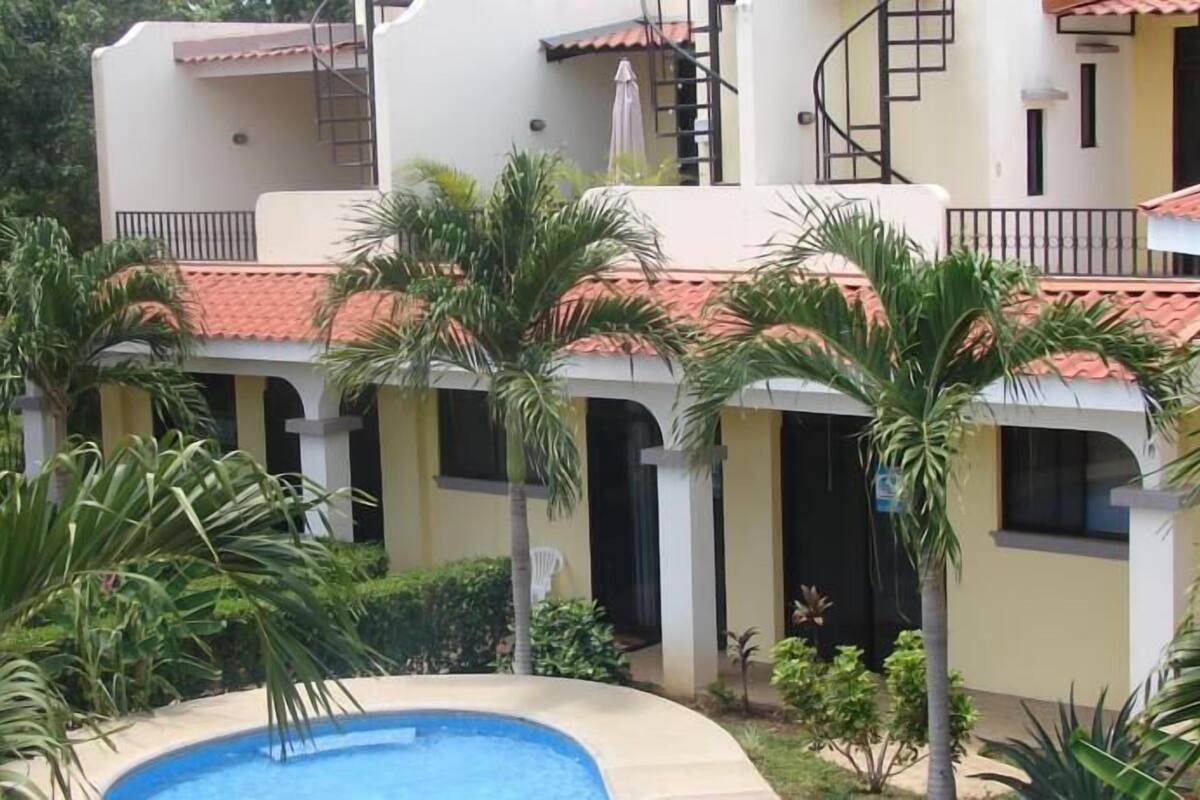 A building with multiple balconies, a swimming pool, and lush greenery.