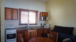 A compact kitchen with a microwave, oven, and sink. There is a dining table with chairs and a sofa in the living area. - Las Torres Studio (Sardinal)
