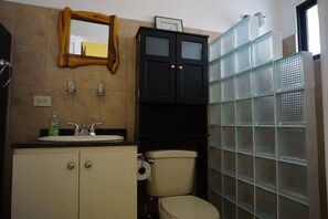 Kylpyhuone, jossa on pesuallas, peili, wc ja suihkukaappi lasiovella.