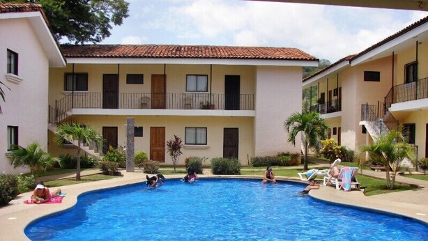 A swimming pool surrounded by a building with balconies and a tiled roof. - Las Torres Studio (Sardinal)
