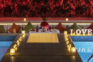A poolside dining area with a table set for two, candles, and a floral centerpiece.