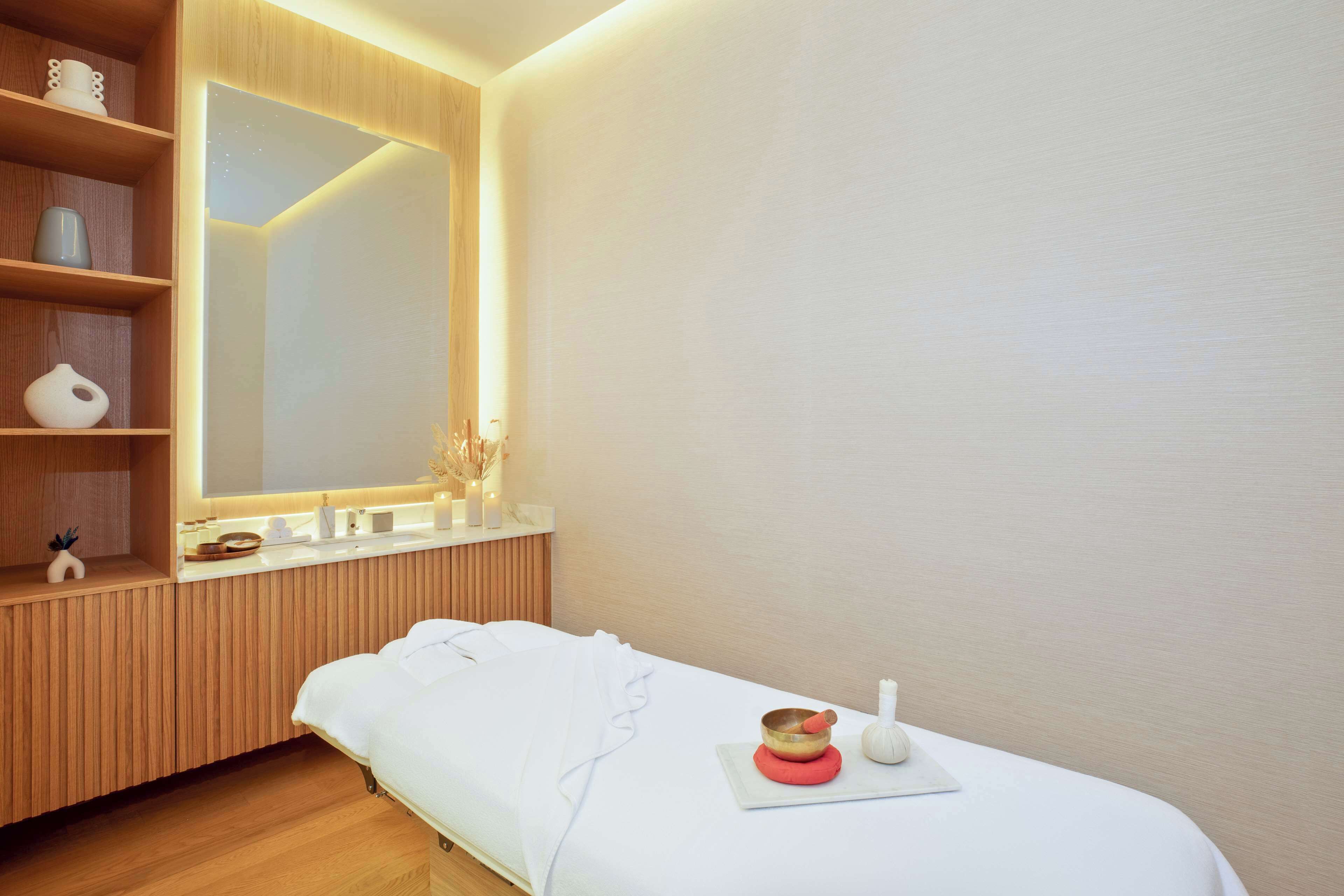 Un dormitorio moderno y minimalista con un tocador de madera, un espejo grande y una mesa de masaje con una colchoneta roja y un tazón.