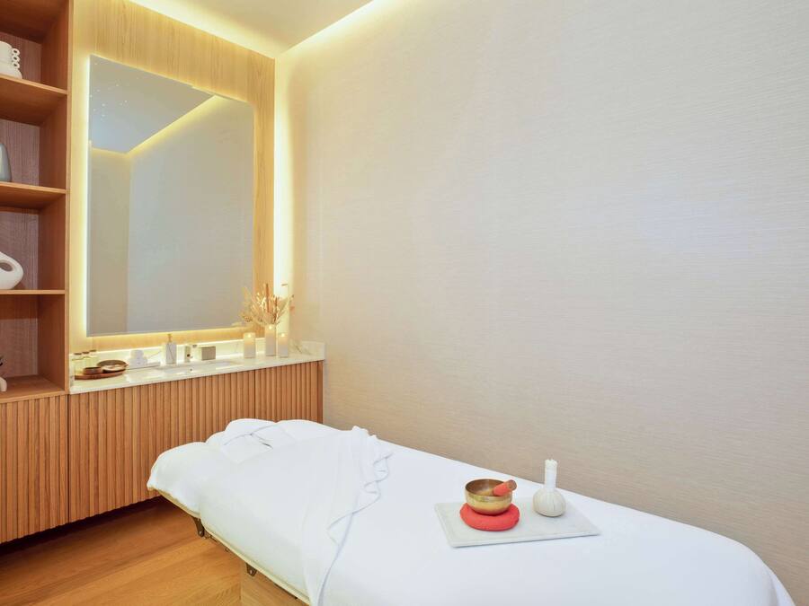 Un dormitorio moderno y minimalista con un tocador de madera, un espejo grande y una mesa de masaje con una colchoneta roja y un tazón.