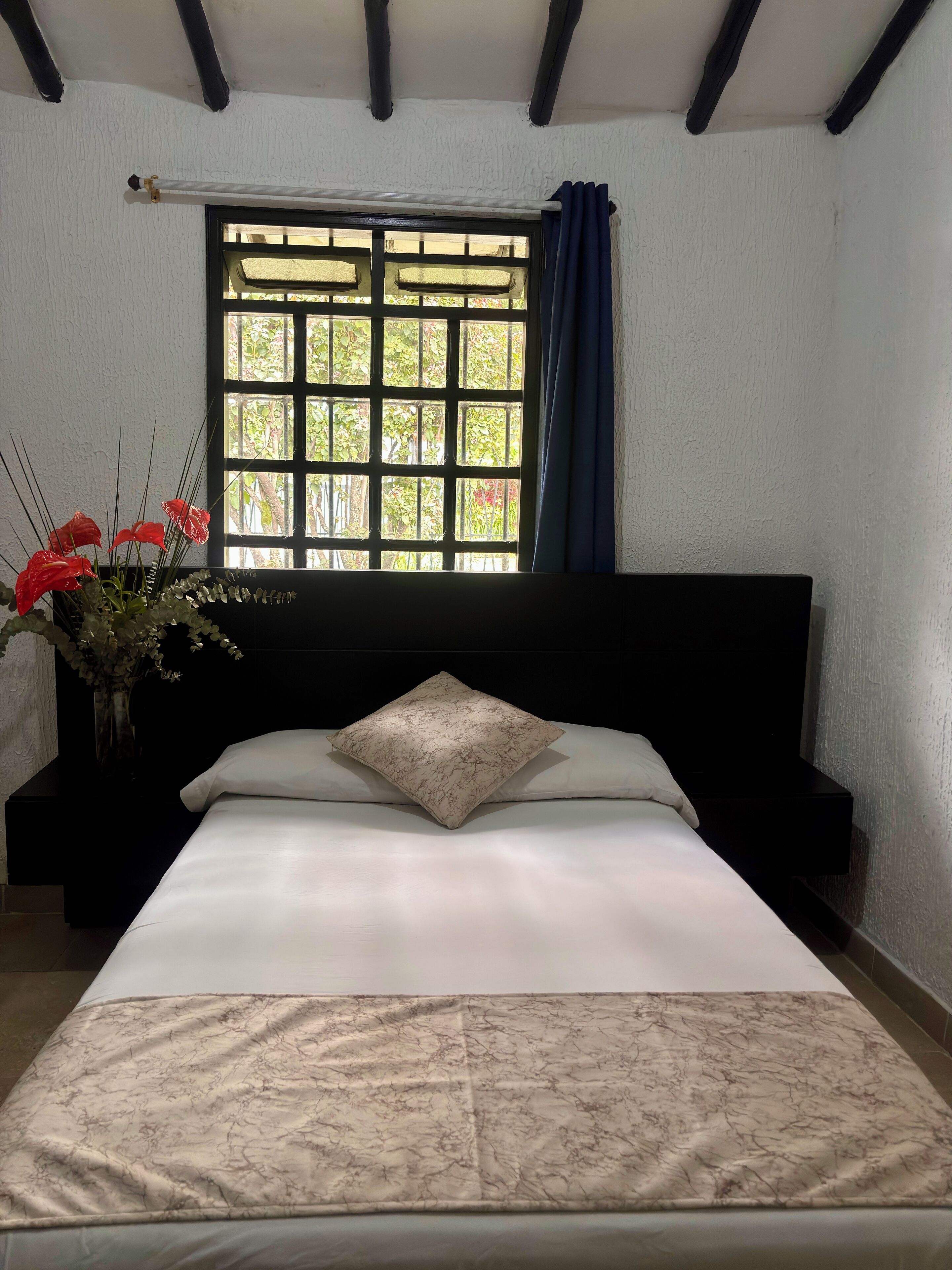 Ein Schlafzimmer mit einem Bett, einem Fenster mit Vorhängen und einer Vase mit Blumen.