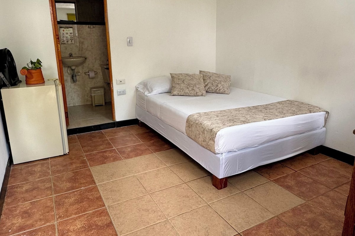 Une chambre à coucher avec un lit, un petit bureau et une salle de bain visible à travers une porte ouverte.