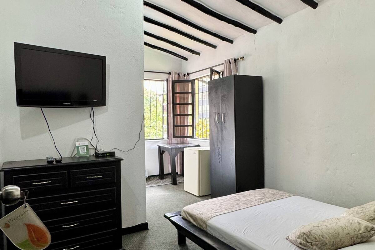 Une chambre à coucher comprenant un lit, une commode, un téléviseur et un petit réfrigérateur.