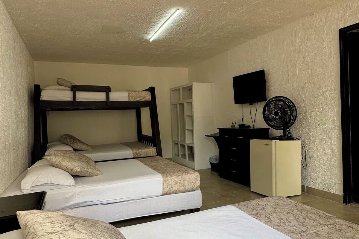 Une chambre de type dortoir, équipée de lits superposés, d’un bureau, d’une télévision et d’un ventilateur.