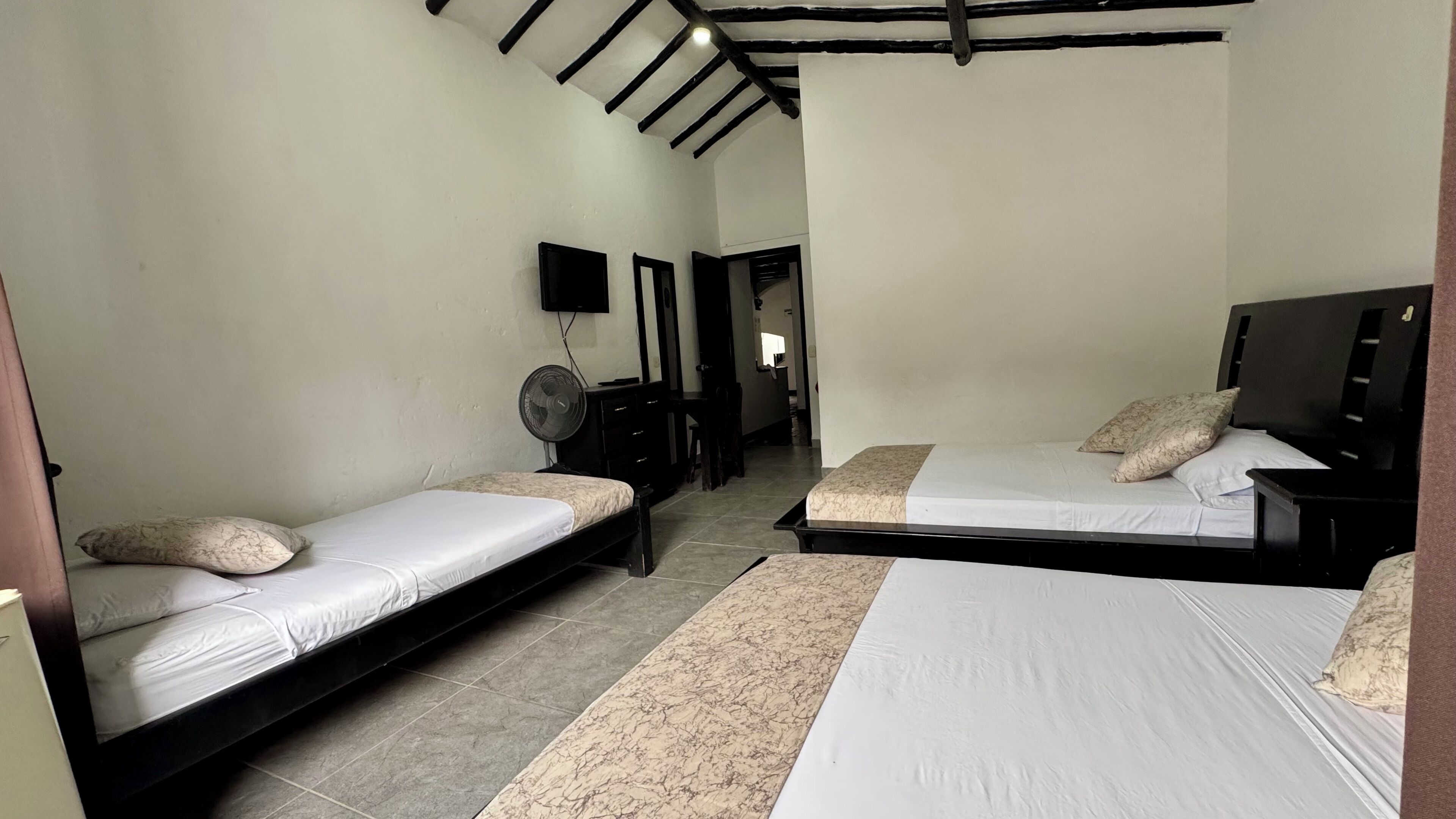 A bedroom with two single beds, a desk, a chair, a TV, and a fan.