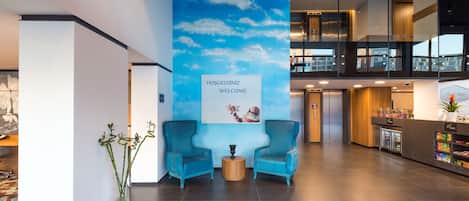 A modern lobby with a blue sky mural, two blue armchairs, a reception desk, and a vending machine.