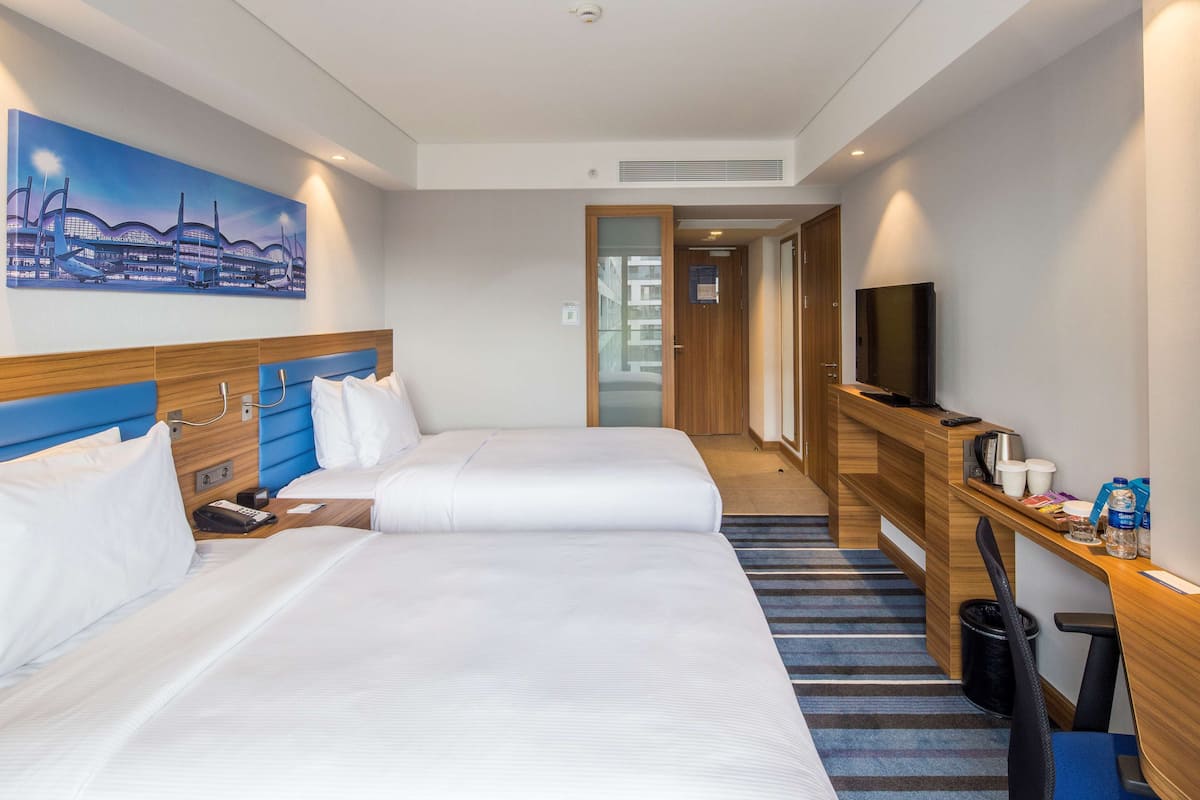 A hotel room with two beds, a desk with a TV, and a painting on the wall.