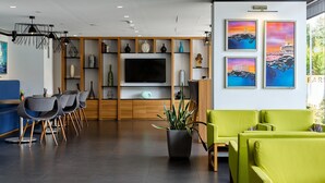 A modern hotel lobby with a large flat-screen TV, wooden paneling, green and gray seating, and artwork on the walls. - Hampton by Hilton Istanbul Kurtkoy (Istanbul)