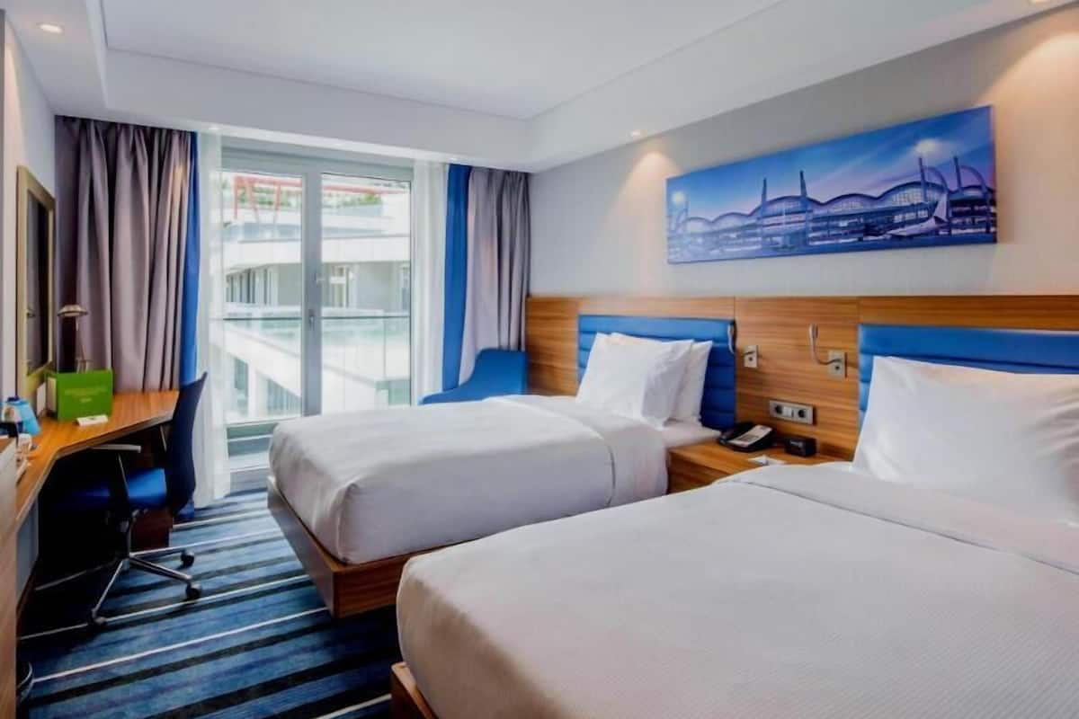 A hotel room with two beds, a desk, a chair, a phone, and a painting on the wall.