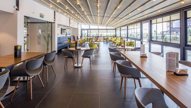 A modern cafeteria with long tables and chairs, large windows, and a clean, organized layout. - Hampton by Hilton Istanbul Kurtkoy (Istanbul)