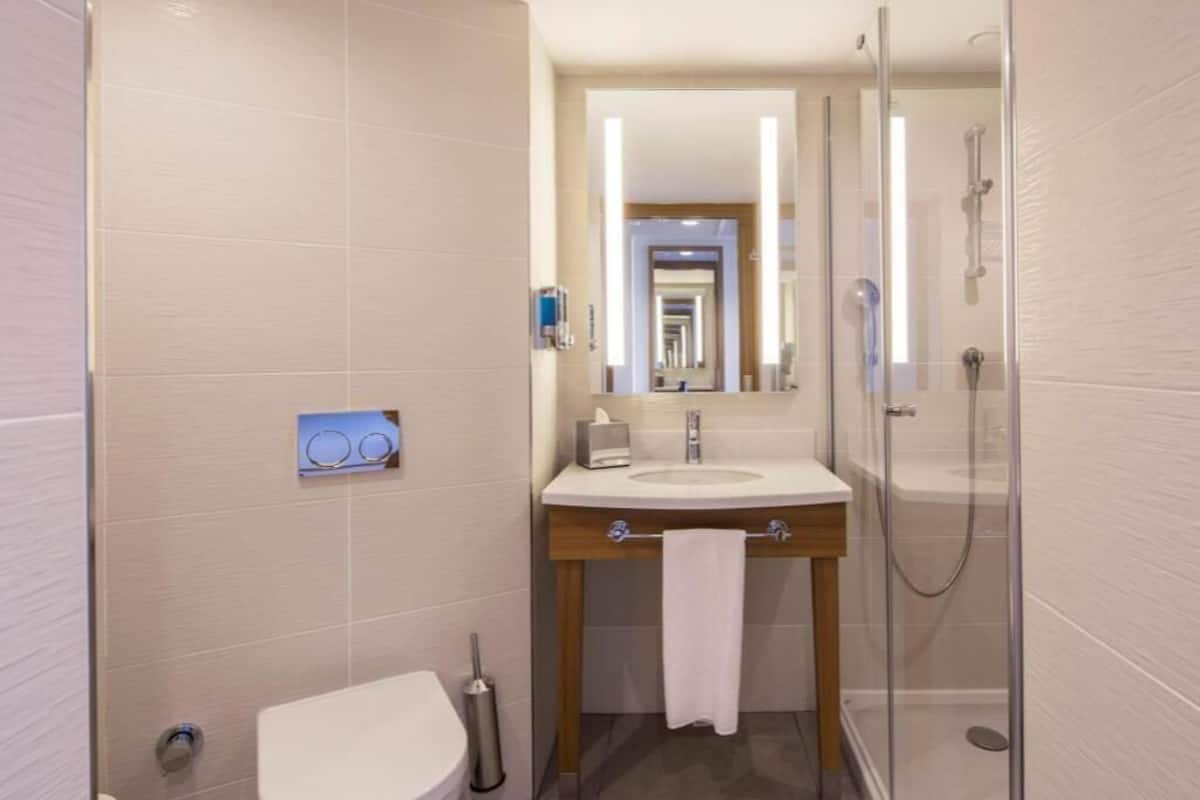 A bathroom with a toilet, sink, mirror, and shower.