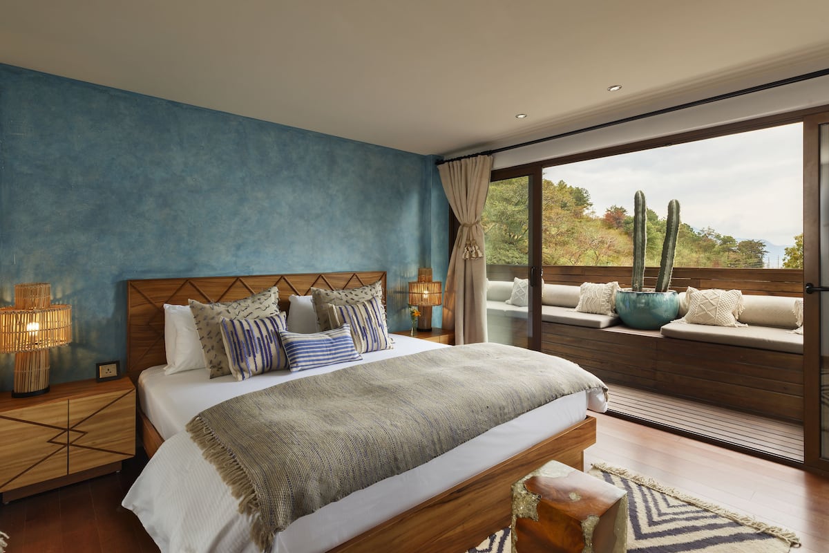 Une chambre avec un grand lit, une tête de lit en bois et une vue sur des cactus, visible à travers une porte-fenêtre coulissante.