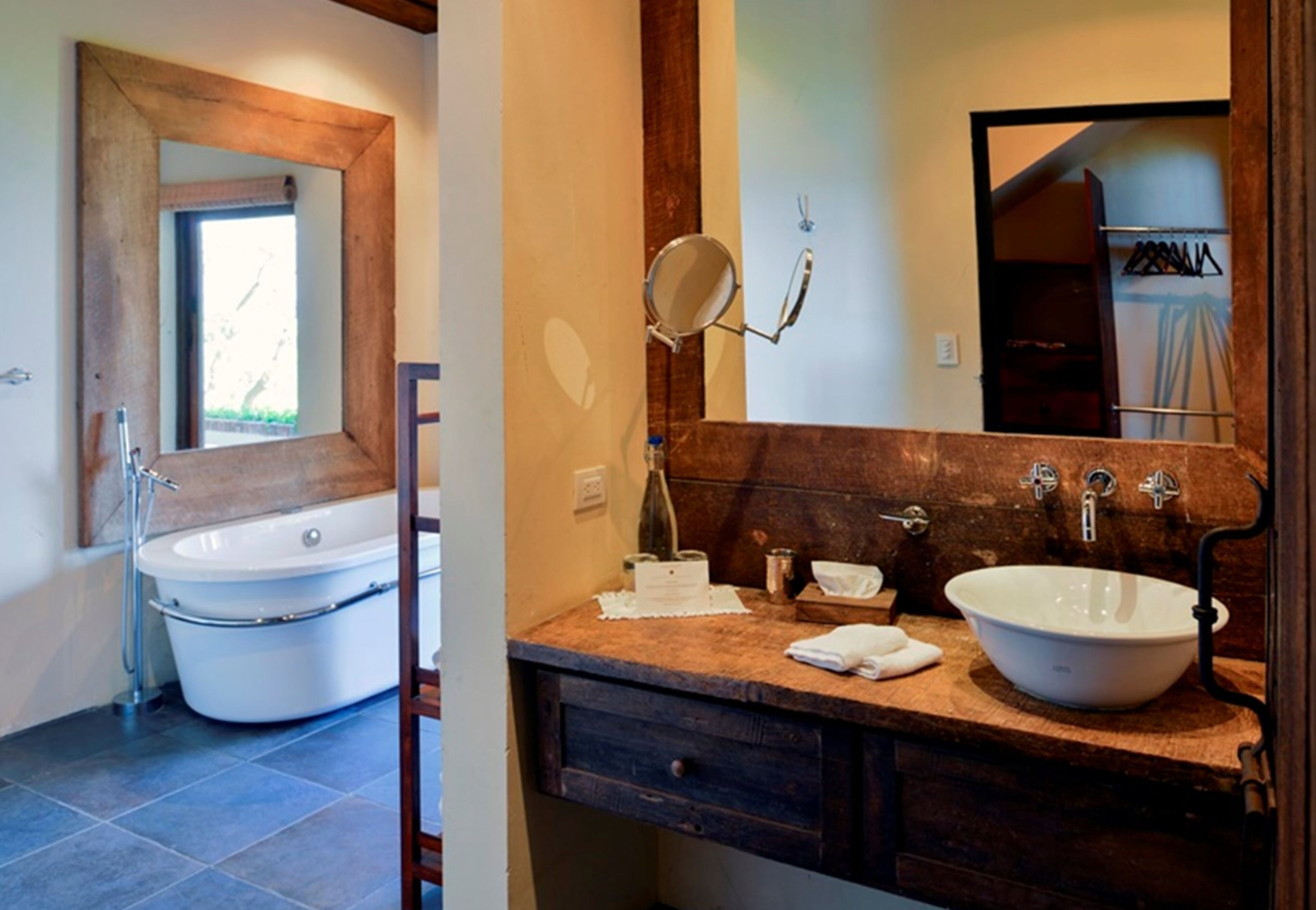 A bathroom with a freestanding bathtub, a large mirror, a wooden vanity with a sink, and a towel on the counter.