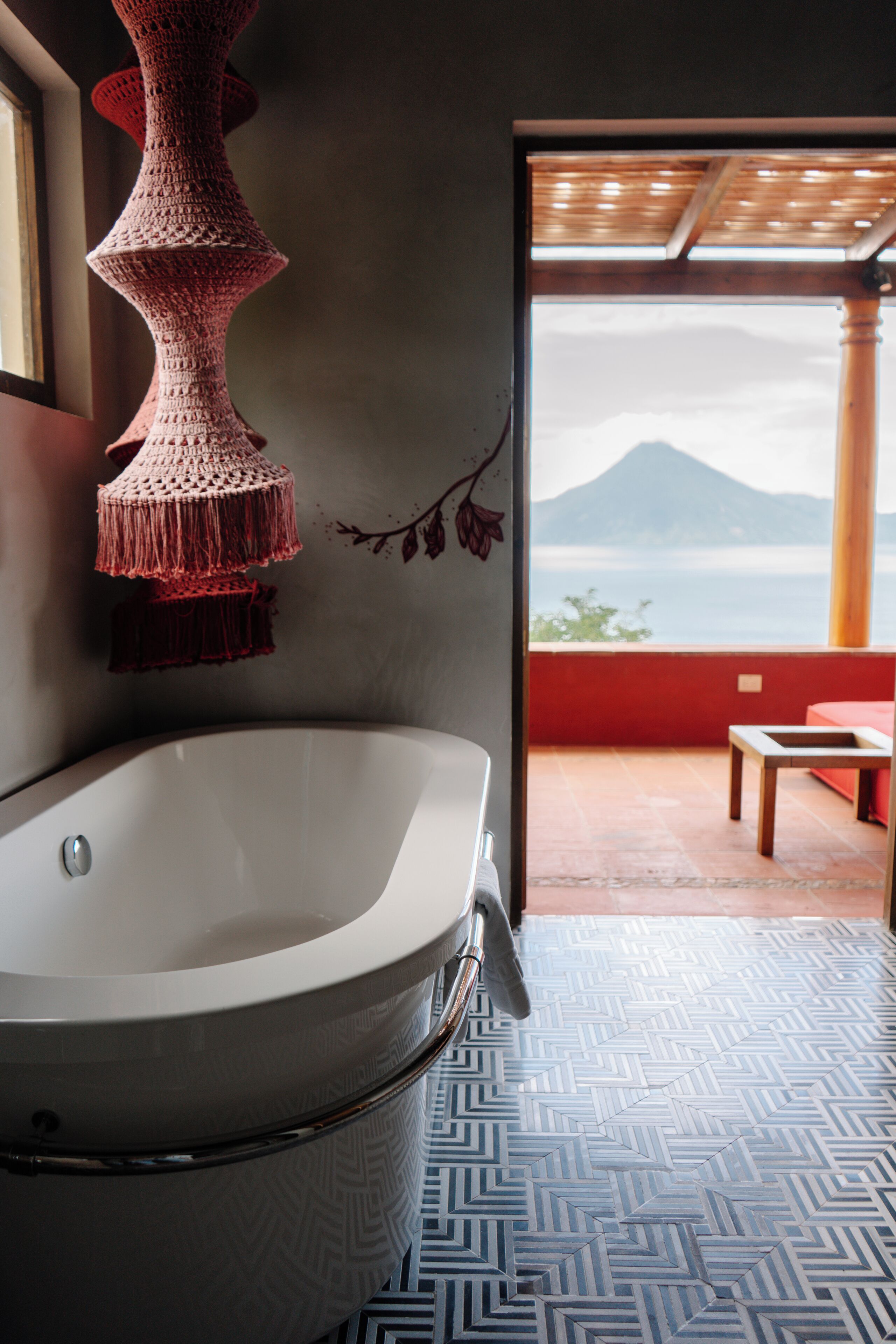 Un baño con una bañera grande, una lámpara colgante de ganchillo y vistas a la montaña a través de una puerta abierta.