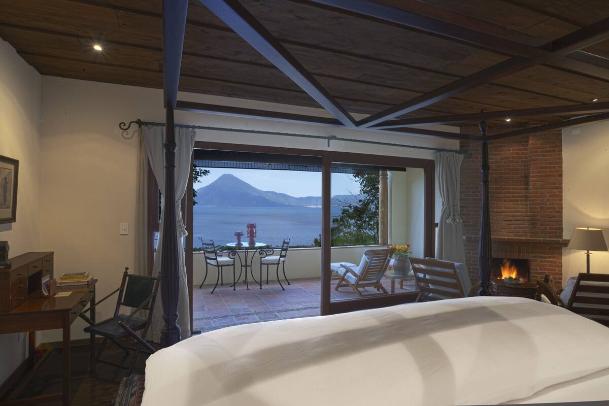 Une chambre à coucher avec un grand lit, une cheminée, un balcon donnant sur une montagne et une table avec des chaises.