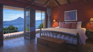 Une chambre avec un grand lit, une table de chevet, une lampe et une vue sur la mer et les montagnes.