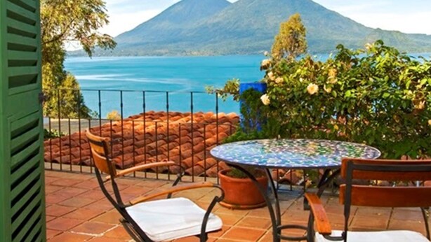 Une terrasse avec une table ronde et des chaises, offrant une vue sur une montagne et un lac.
