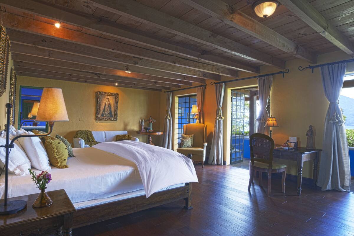 Une chambre spacieuse avec un grand lit, un bureau et une chaise. Il y a une fenêtre avec des rideaux et une vue sur l’extérieur.