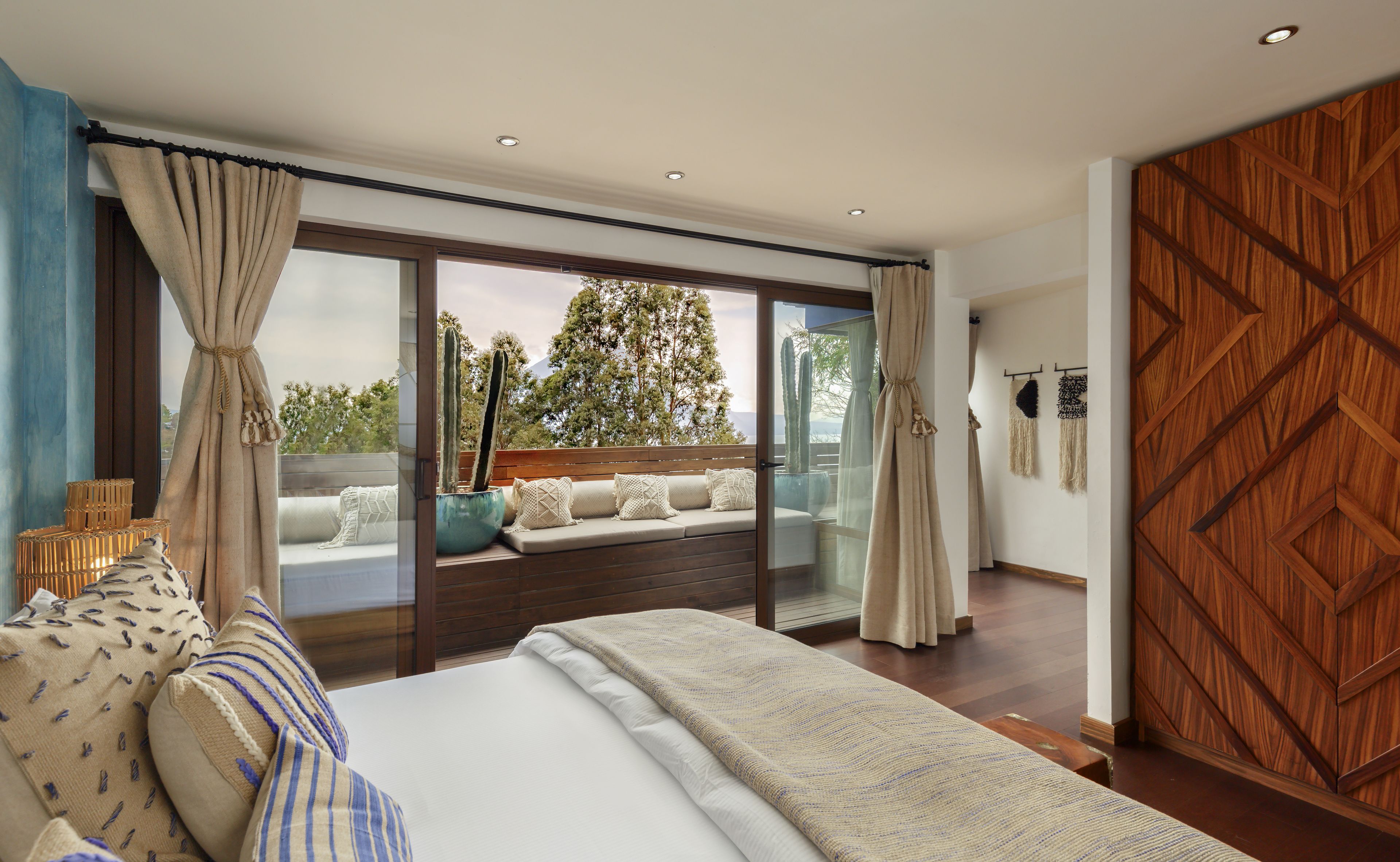 Un dormitorio con una cama grande, vistas a árboles y una montaña a través de ventanas de gran altura, y un armario de madera.
