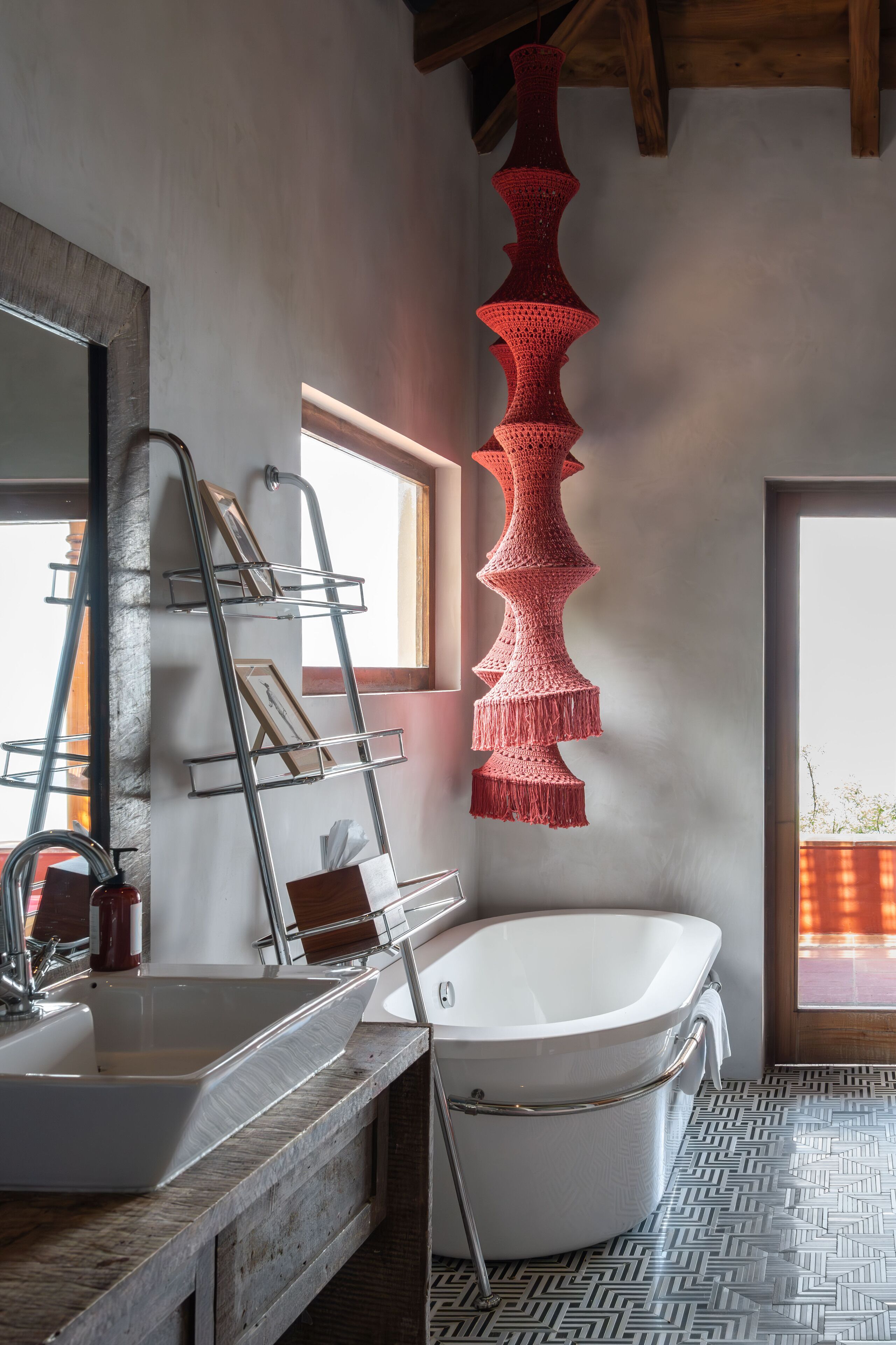 A modern bathroom with a freestanding bathtub, a metal shelf unit, and a red macramé wall hanging.